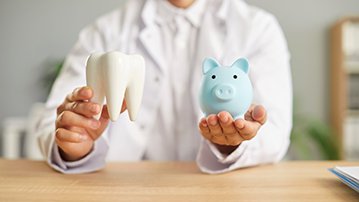 Dentist in white coat holding a piggy bank and large model tooth