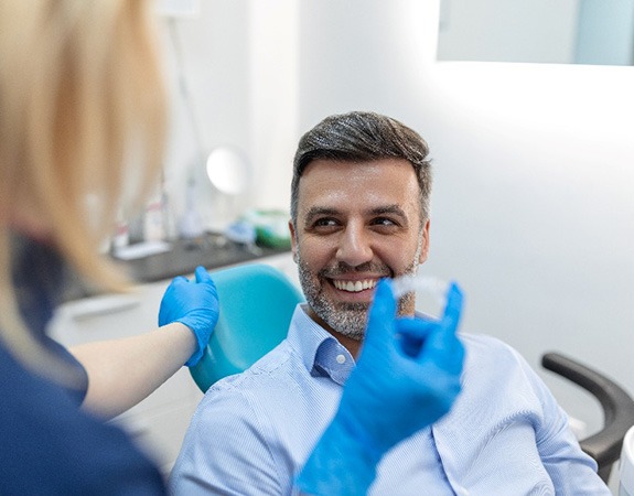 Man smiling at dental assistant who is holding an Invisalign aligner
